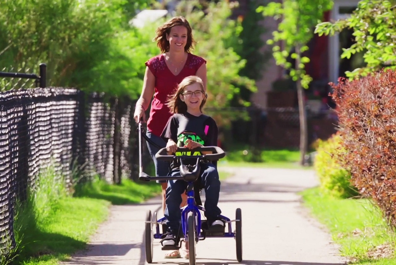 Kind im Rollstuhl, dass von einer Betreuungsperson spazieren gefahren wird wird